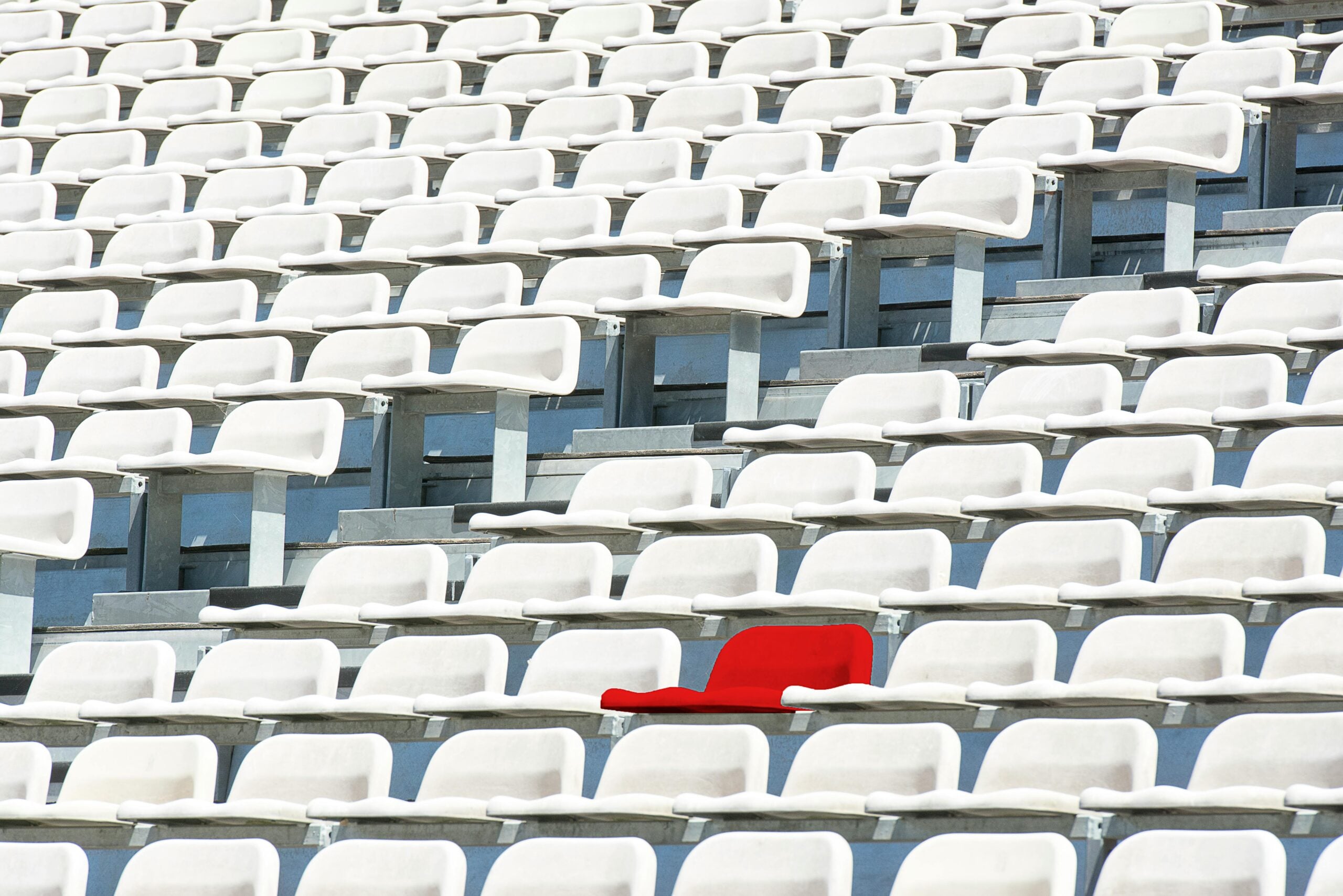 Single red seat among rows of white stadium seats